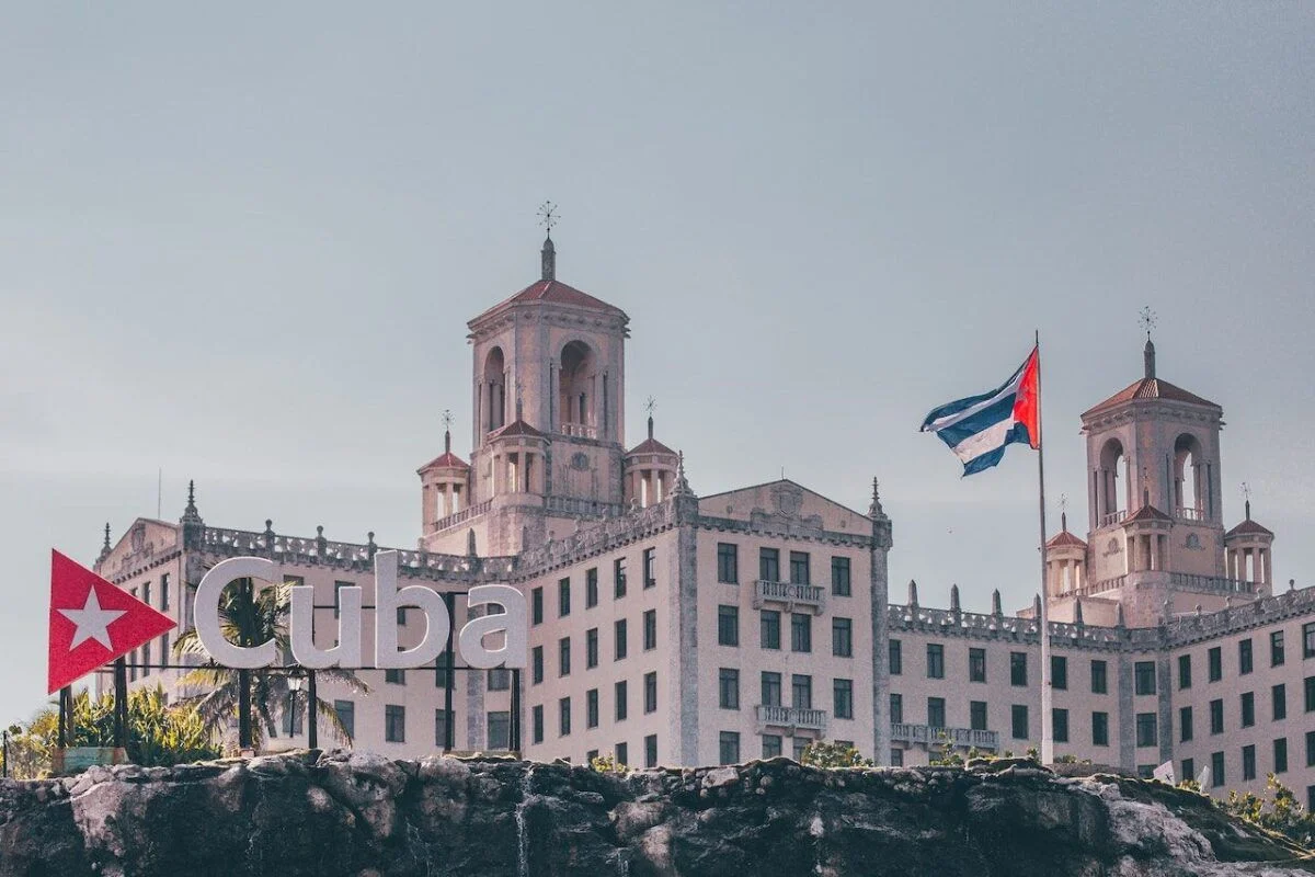The historic Hotel Nacional de Cuba in Havana, with a Cuban flag flying and a large “Cuba” sign in the foreground.