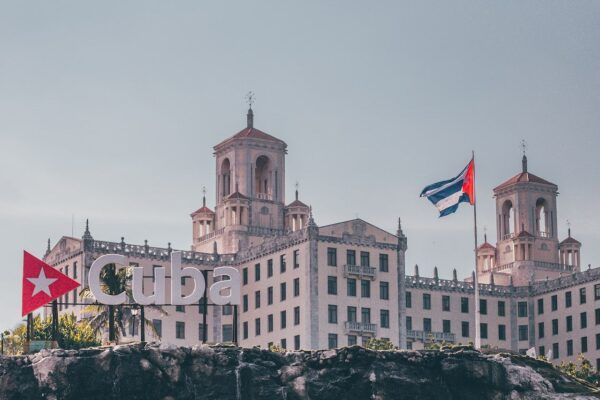 The historic Hotel Nacional de Cuba in Havana, with a Cuban flag flying and a large “Cuba” sign in the foreground.