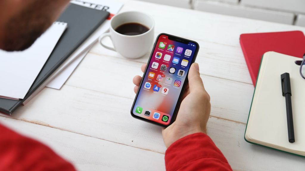 The Impact Of Beacon Technology On The Gambling Industry 2 A person holding a smartphone displaying a home screen filled with app icons, sitting at a desk with a coffee cup, notebooks, and a pen.