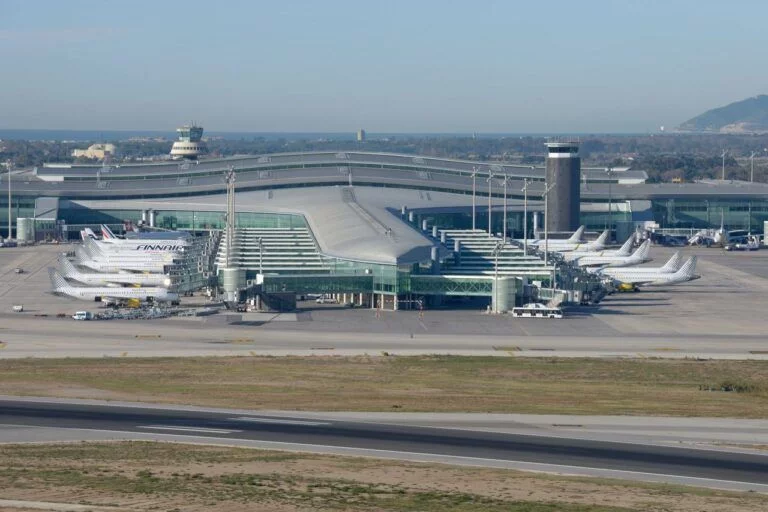 Aerial view of Barcelona El Prat Airport terminal with multiple aircraft parked at the gates.