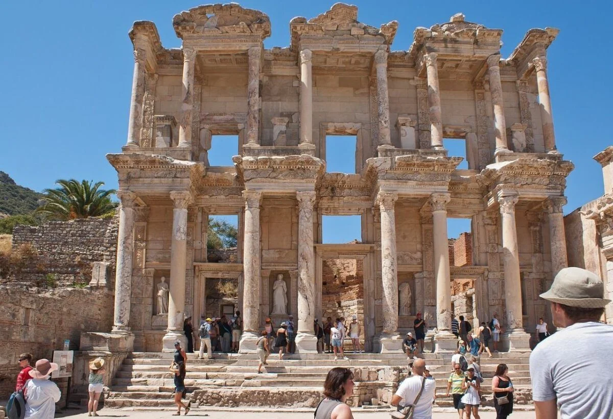 Tourists explore the ancient ruins of the Library of Celsus in Ephesus, Turkey, on a sunny day with a clear blue sky.