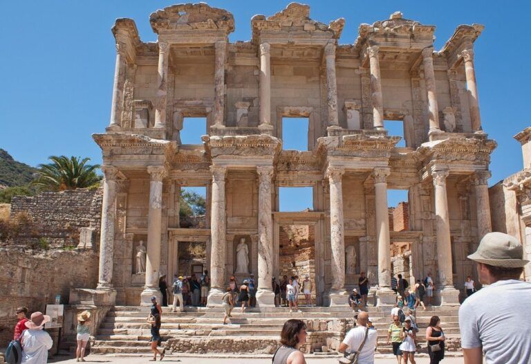 Tourists explore the ancient ruins of the Library of Celsus in Ephesus, Turkey, on a sunny day with a clear blue sky.