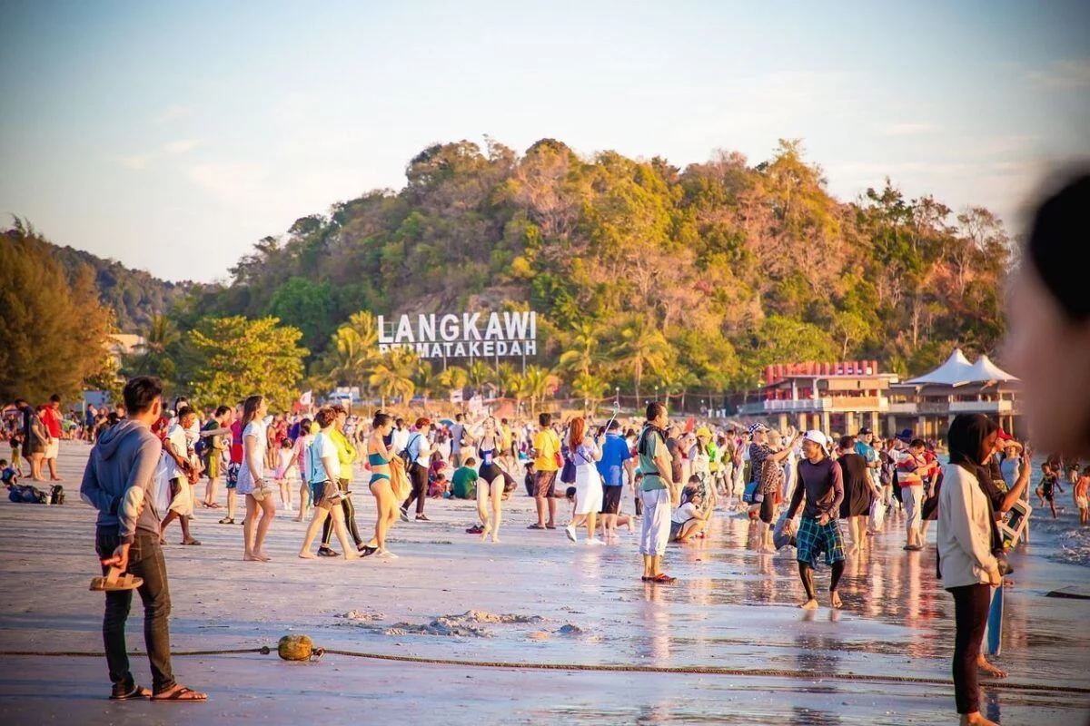 A crowded beach in Langkawi, Malaysia, with tourists enjoying the sunset.