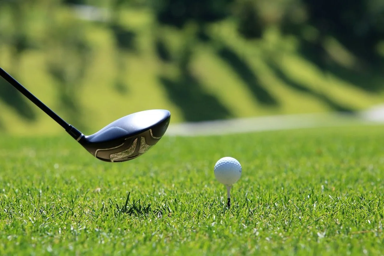 Close-up of a golf club poised to hit a golf ball on a tee.