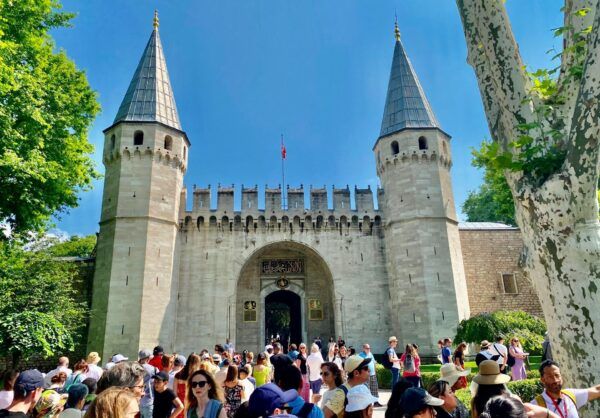 Turkiye 11 Tourists gathered at the entrance gate of Topkapı Palace in Istanbul, with its iconic towers and historic architecture under a bright blue sky.