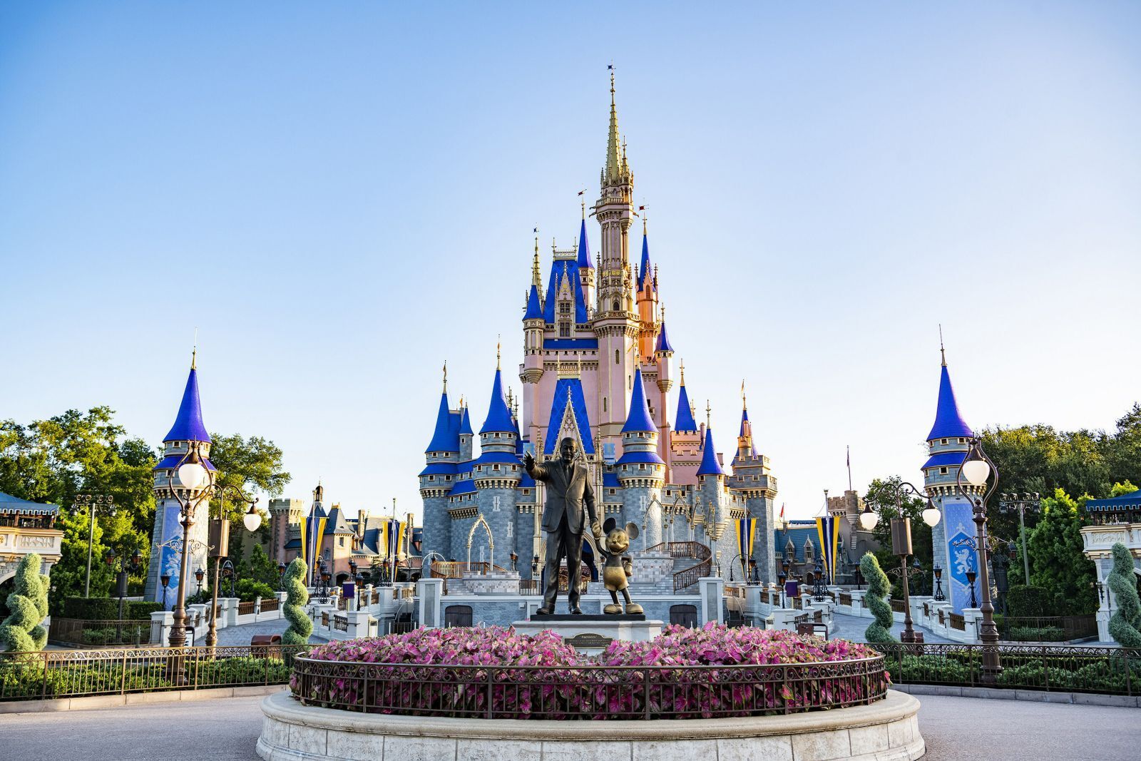 Cinderella Castle at Walt Disney World in Florida, with the Partners Statue of Walt Disney and Mickey Mouse in the foreground, surrounded by vibrant flowers and clear blue skies.