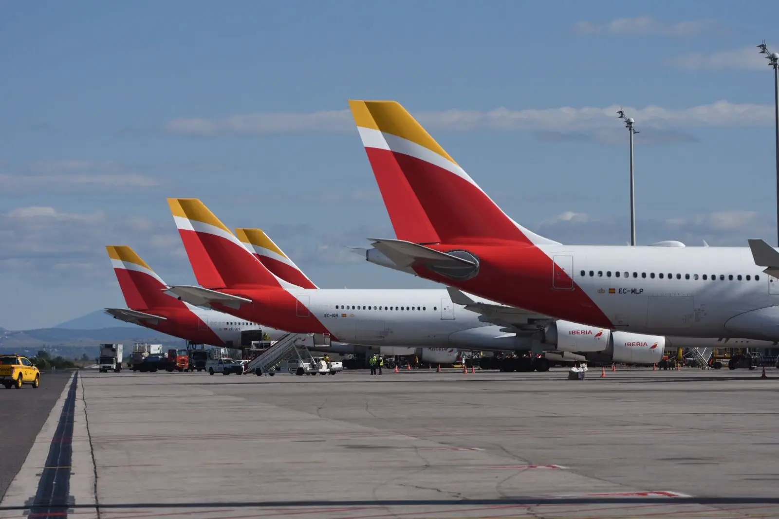 Row of Iberia aircraft with red and yellow tails parked on the tarmac.