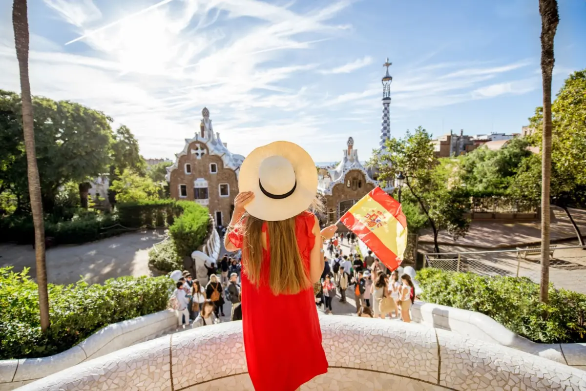 red dressed woman tourist visits Barcelona's Park Guell, holding a Spanish flag in a sunny warm day