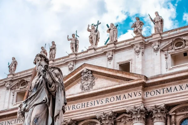 Close-up view of St. Peter’s Basilica in Vatican City, showcasing intricate statues of apostles and saints on the facade against a partly cloudy sky.
