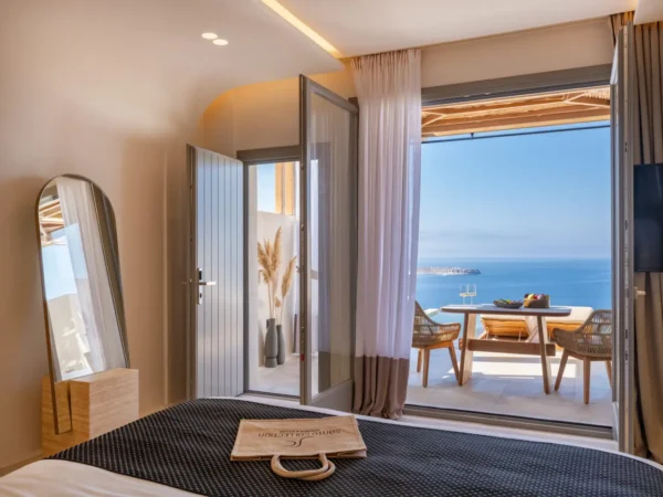 New Greece Hotel in Santorini. Guestroom with bed with stunning seaview and terrace with a table at Santo Mine Oia Suites