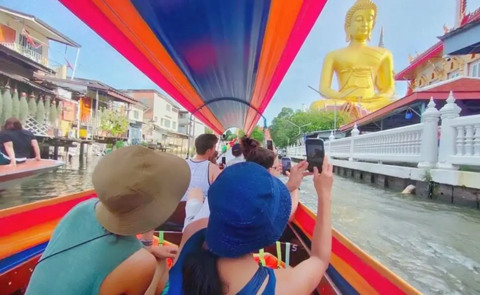 Tourists on riverboat in Thailand taking photo of the Golden Budha