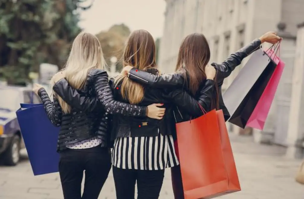 three women hug each other returning from shopping by carrying shopping bags