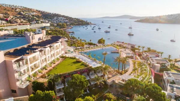 Home 13 Aerial view of Baia Bodrum, a luxury resort in Bodrum, Turkey, overlooking the Aegean Sea with yachts anchored in the bay and lush greenery surrounding the property.
