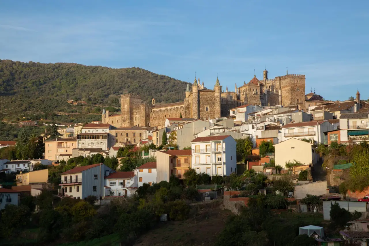 Scenic view of the historic town of Guadalupe in Cáceres Province, Spain, featuring a medieval monastery and traditional Spanish architecture set against a backdrop of lush green hills.