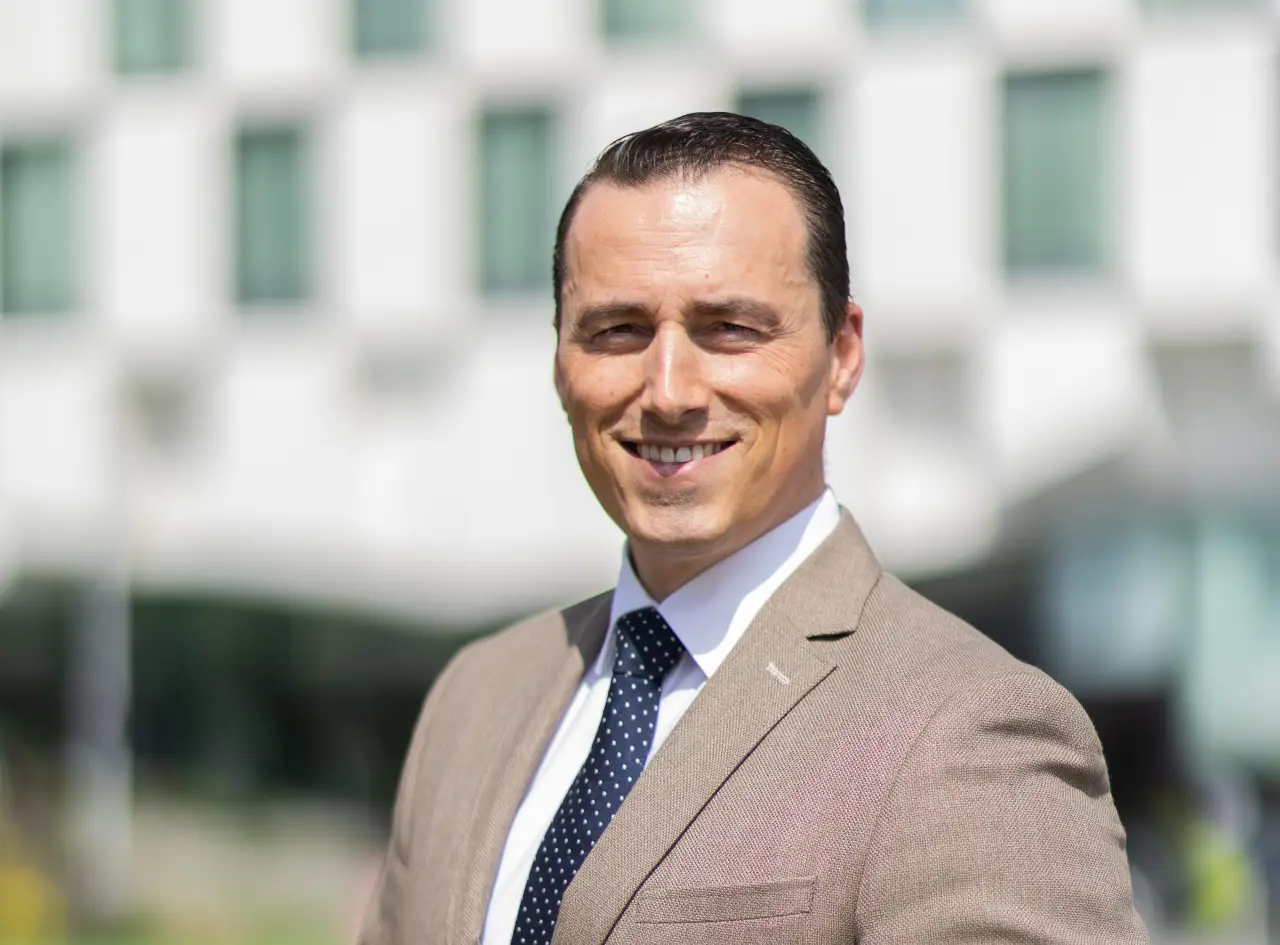 Ludo de Jong, the newly appointed General Manager of Anantara The Marker Dublin Hotel, smiling while standing outdoors in a beige suit with a white shirt and navy polka dot tie.