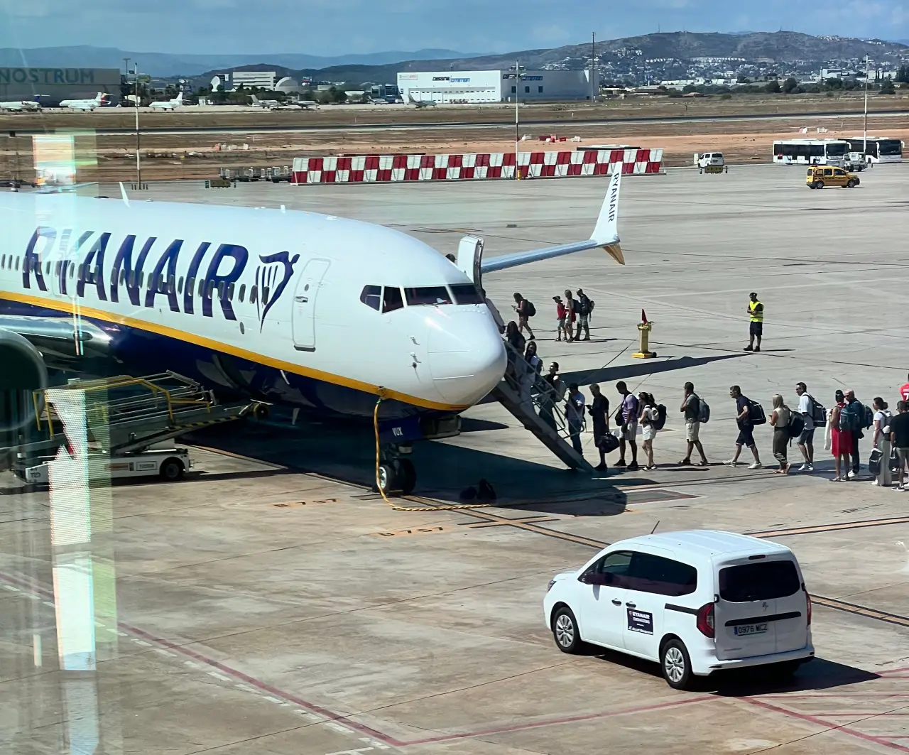 Passengers boarding a Ryanair plane on the tarmac at Valencia Airport, with a white airport service vehicle nearby.