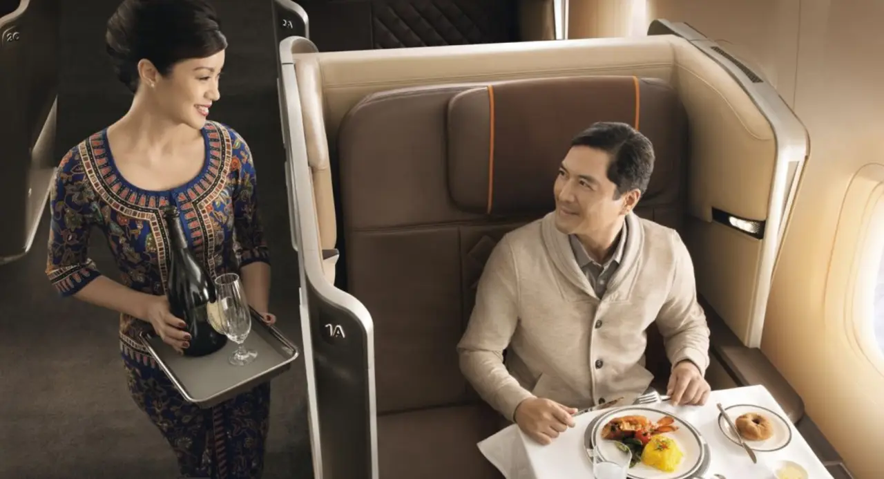 Singapore Airlines flight attendant serving a meal to a passenger in a luxurious first-class cabin.