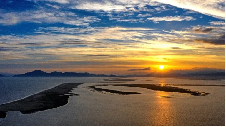 A stunning sunset over the Nakdong Estuary in Busan, with the sun casting a warm golden glow over the water and distant mountains.
