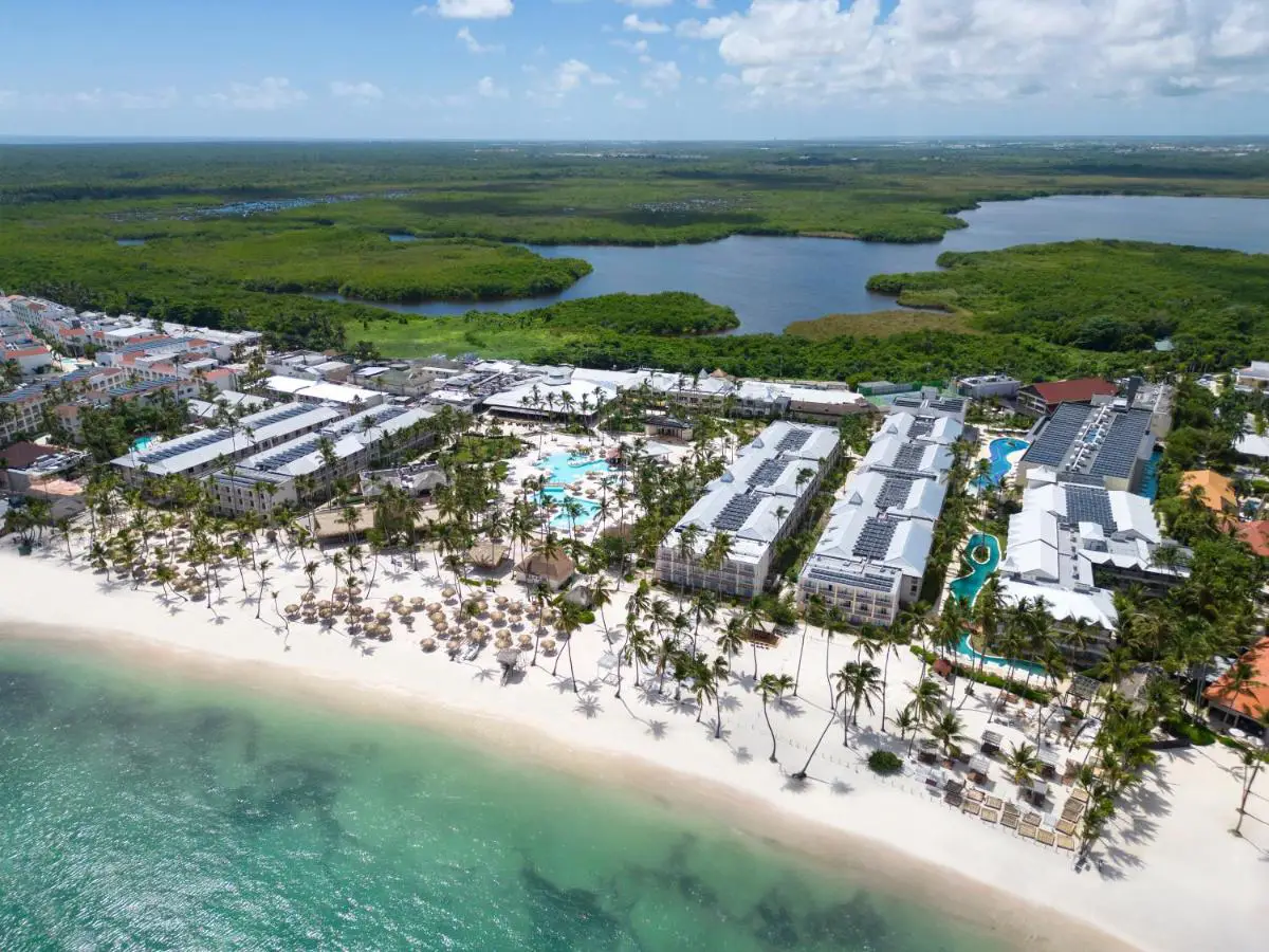 An aerial view of Sunscape Coco Punta Cana Resort, located along the shores of Bavaro Beach, featuring white sand, lush palm trees and turquoise waters.