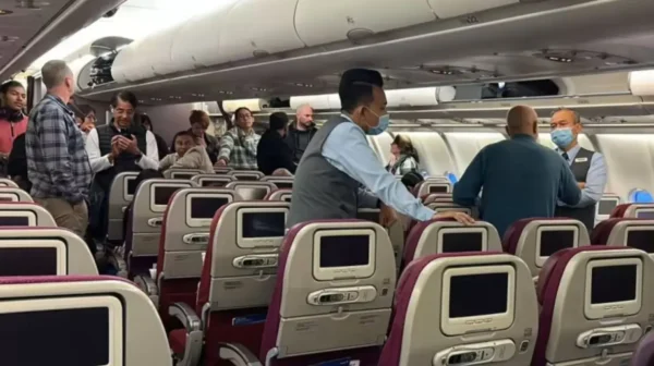 Airline cabin with passengers standing and interacting with flight attendants, some wearing masks.
