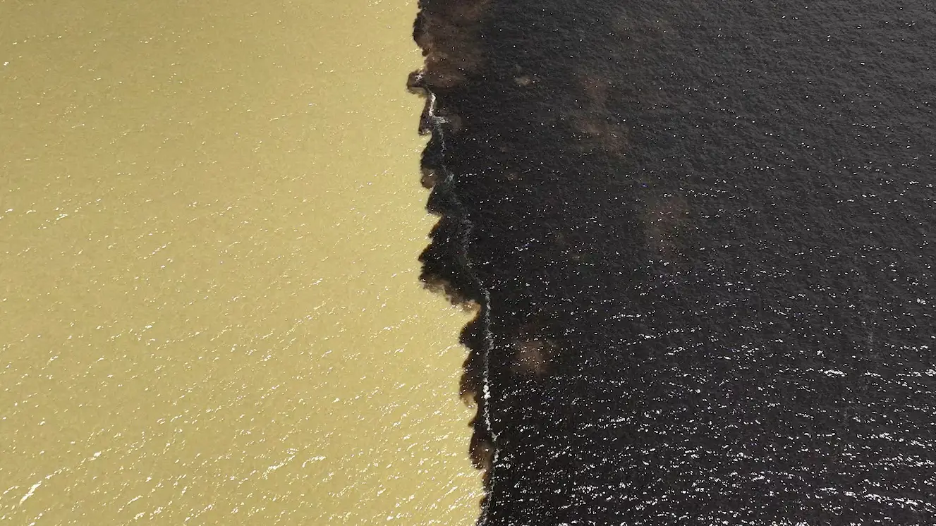 Aerial view of the Meeting of Waters in Manaus, Brazil, where the dark Rio Negro and sandy-colored Rio Solimões flow side by side without mixing.