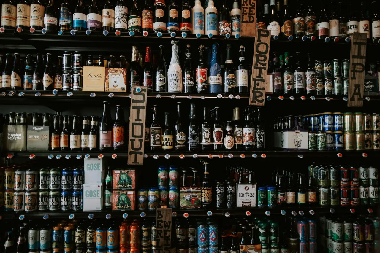 A large shelf displaying a diverse selection of craft beers, including bottles and cans, neatly arranged and labeled with various beer styles like IPA, Stout, and Porter.