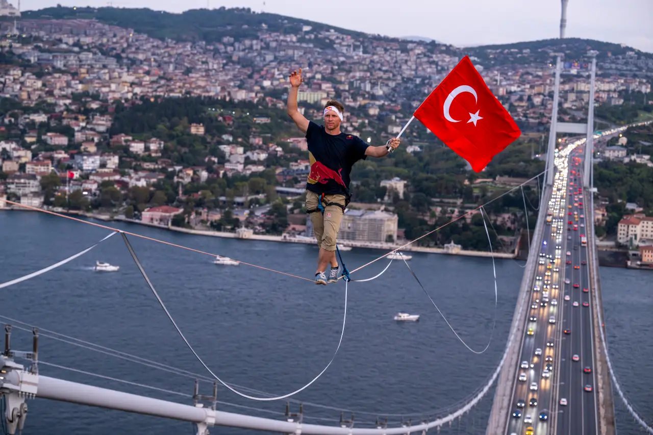 Jaan Roose walking on a slackline across the Bosphorus in Istanbul, holding a Turkish flag.