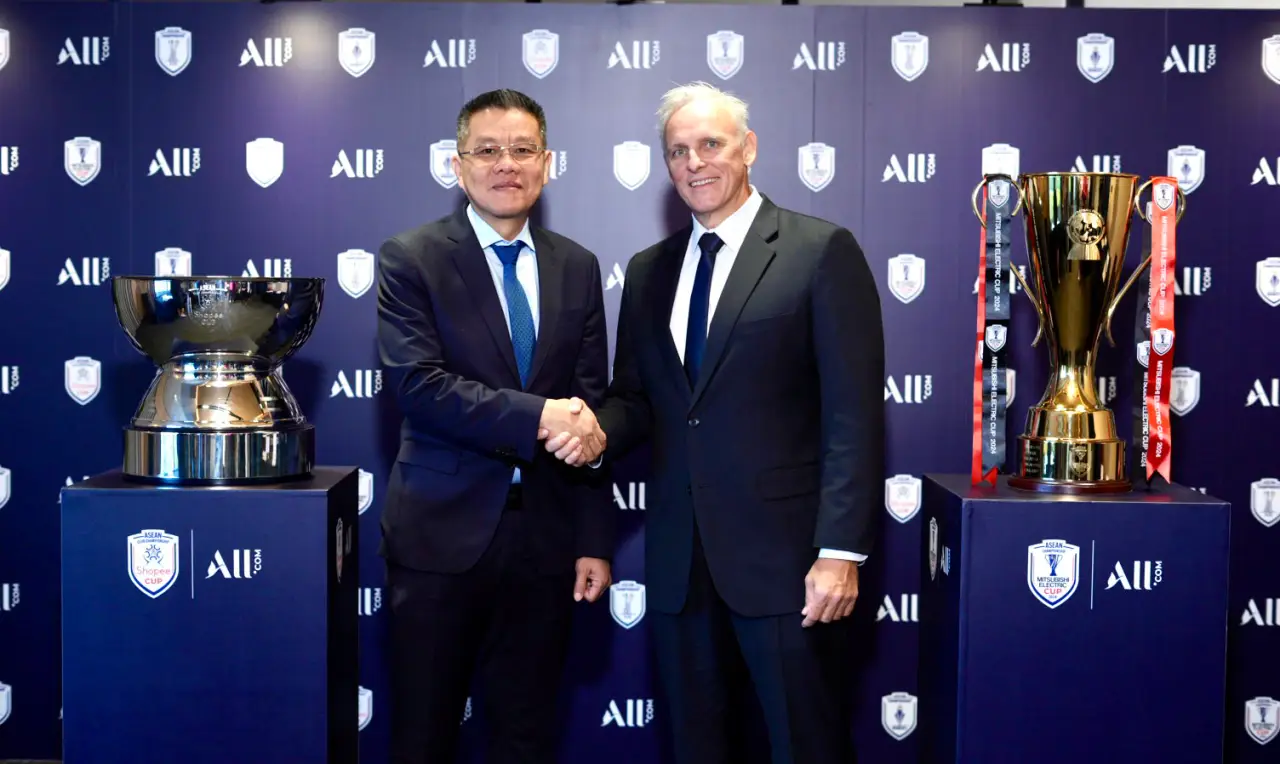 Accor executive and AFF representative shaking hands at the partnership announcement event, with ASEAN football trophies displayed.