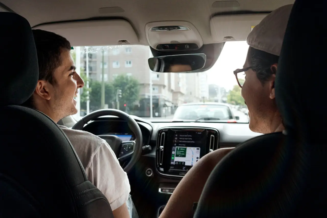 Two people sharing a car ride, smiling and chatting inside a vehicle. The driver and passenger appear to be enjoying a BlaBlaCar ride, with navigation displayed on the car’s central console.