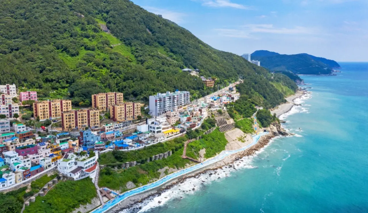 Aerial view of Busan’s coastal neighborhood, with colorful buildings nestled along the hillside and the blue ocean stretching out to the horizon.