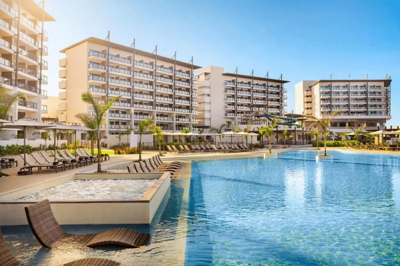 Daytime view of Dreams Estrella del Mar Mazatlán resort showcasing modern buildings, a large pool area, and sun loungers under clear blue skies.