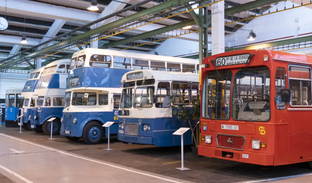 A lineup of historic EMT buses at the current EMT Museum in Madrid, showcasing various models including double-decker and single-decker buses in blue and red colors.