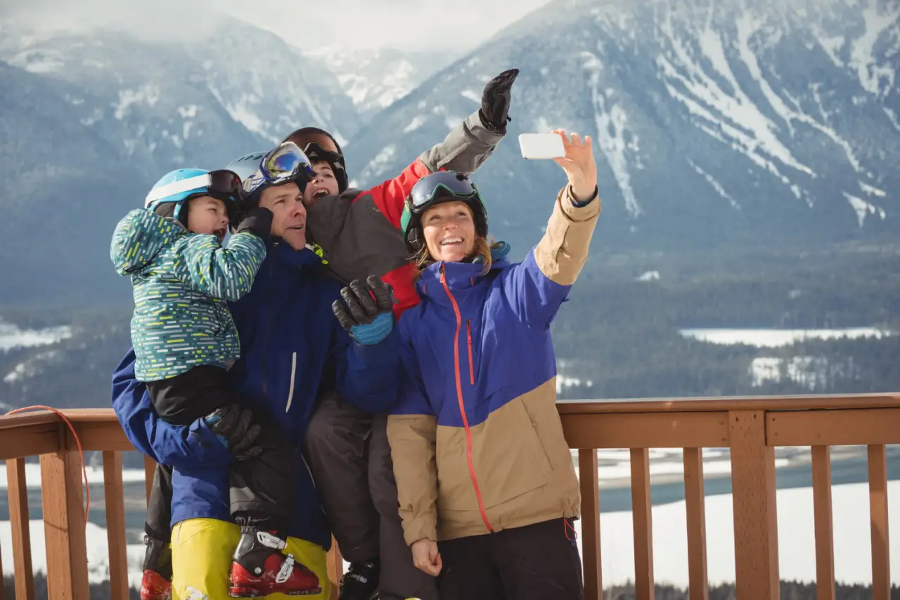 Family taking a selfie at a mountain resort for family ski trips with snow-covered mountains in the background.