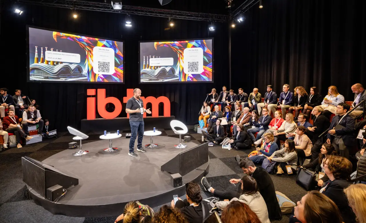 a man on a stage at IBTM Impact forum with a crowd of people watching