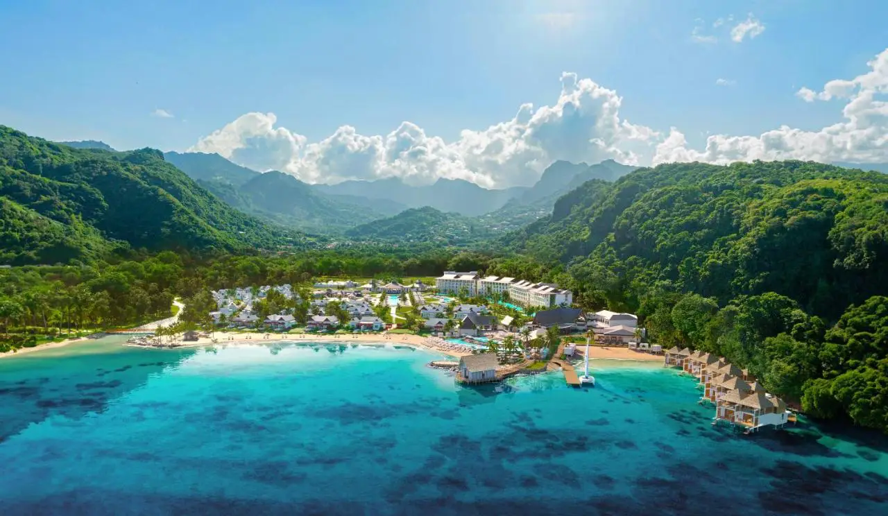 Aerial view of the new all-inclusive resort in the Caribbean, Sandals St. Vincent, nestled along a pristine private cove with lush green mountains in the background and turquoise Caribbean waters in the foreground.