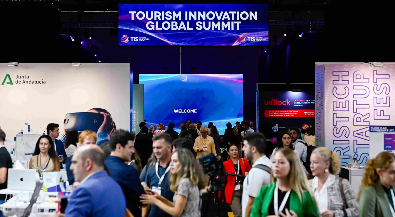 Attendees explore exhibits at the Tourism Innovation Global Summit 2024 in Seville, surrounded by booths and digital displays.