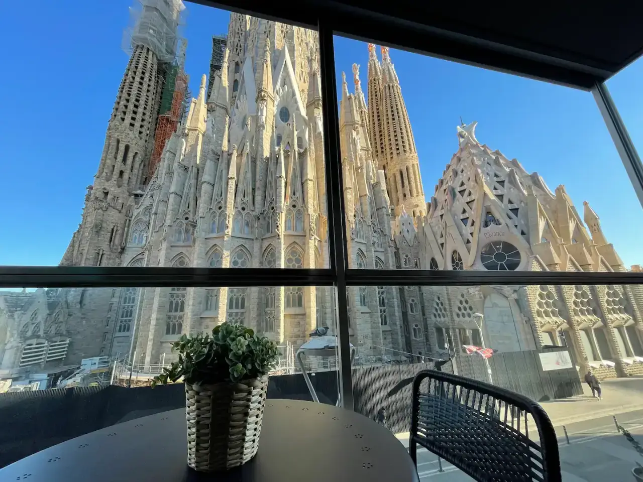 A stunning view of La Sagrada Família from an apartment balcony in Barcelona, with a small plant on the table in the foreground.