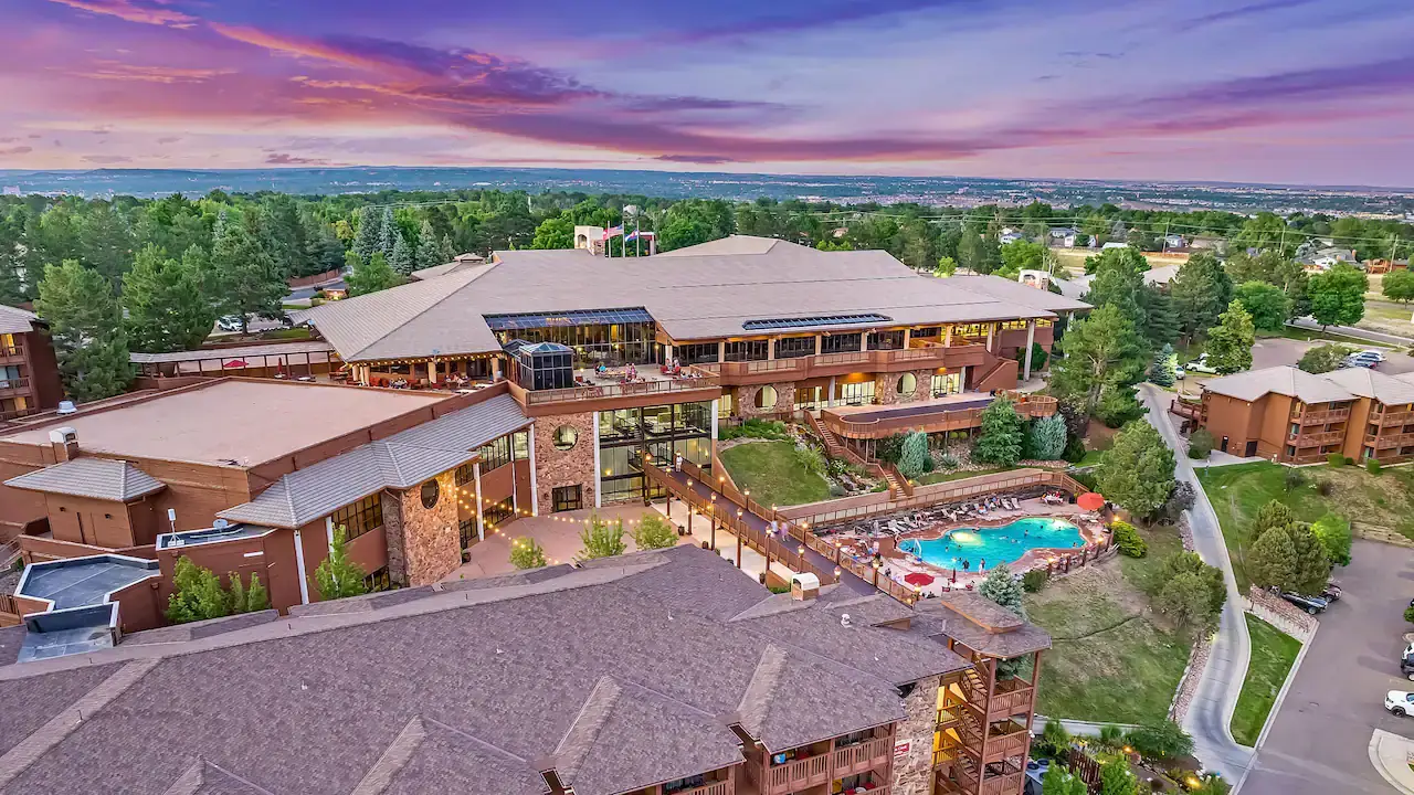 Aerial view of Cheyenne Mountain Resort in Colorado Springs at sunset, with outdoor pool and surrounding greenery.