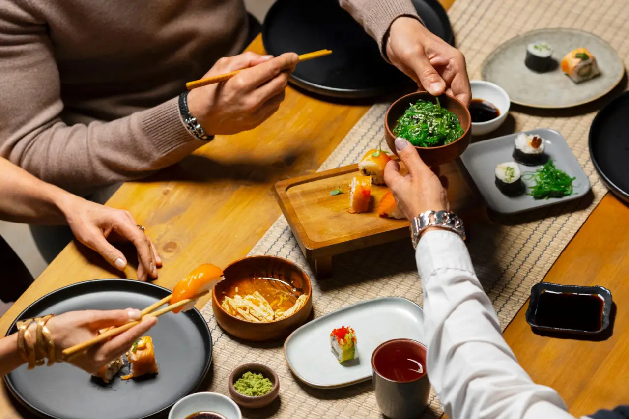 Group of people sharing Asian food at a dining table, enjoying a variety of sushi and side dishes, perfect for exploring foodie destinations.