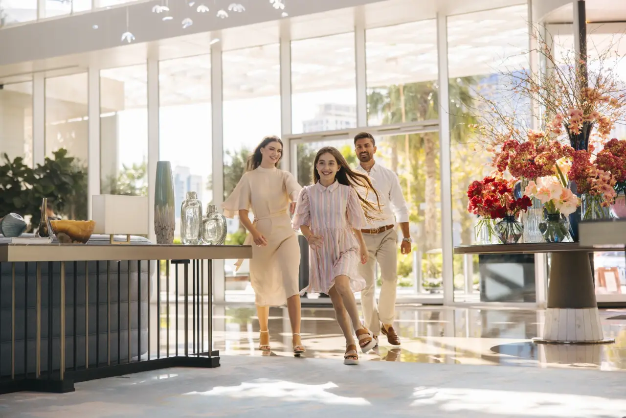 A family joyfully entering a modern, luxurious hotel lobby with vibrant floral arrangements.