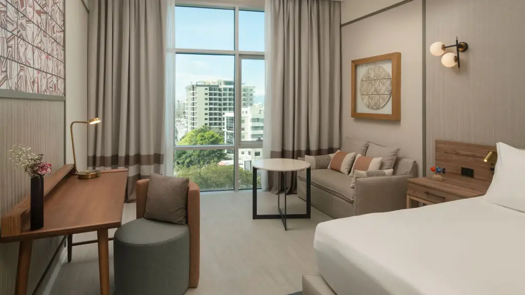 Modern guestroom at Hyatt Centric Santo Domingo with seating area, desk, and city view.