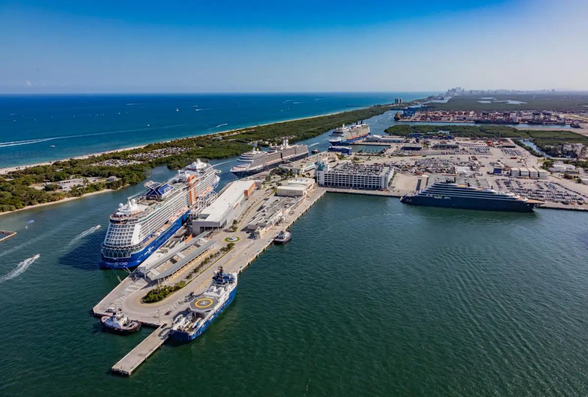 Aerial view of Port Everglades with multiple cruise ships docked along the terminals, set against a backdrop of the ocean and coastline.