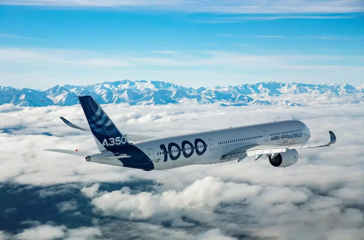 An Airbus A350-1000 aircraft flying above a sea of clouds with snow-capped mountains in the background.