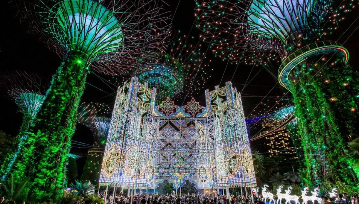 A breathtaking view of Gardens by the Bay in Singapore featuring a magnificent illuminated Spalliera light display and iconic Supertrees lit up at night.