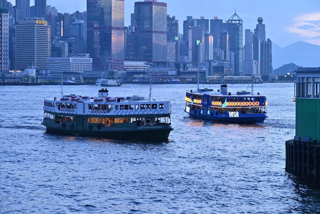 Two ferries on Victoria Harbour with the Hong Kong skyline in the background during twilight, showcasing the city’s vibrant urban landscape.