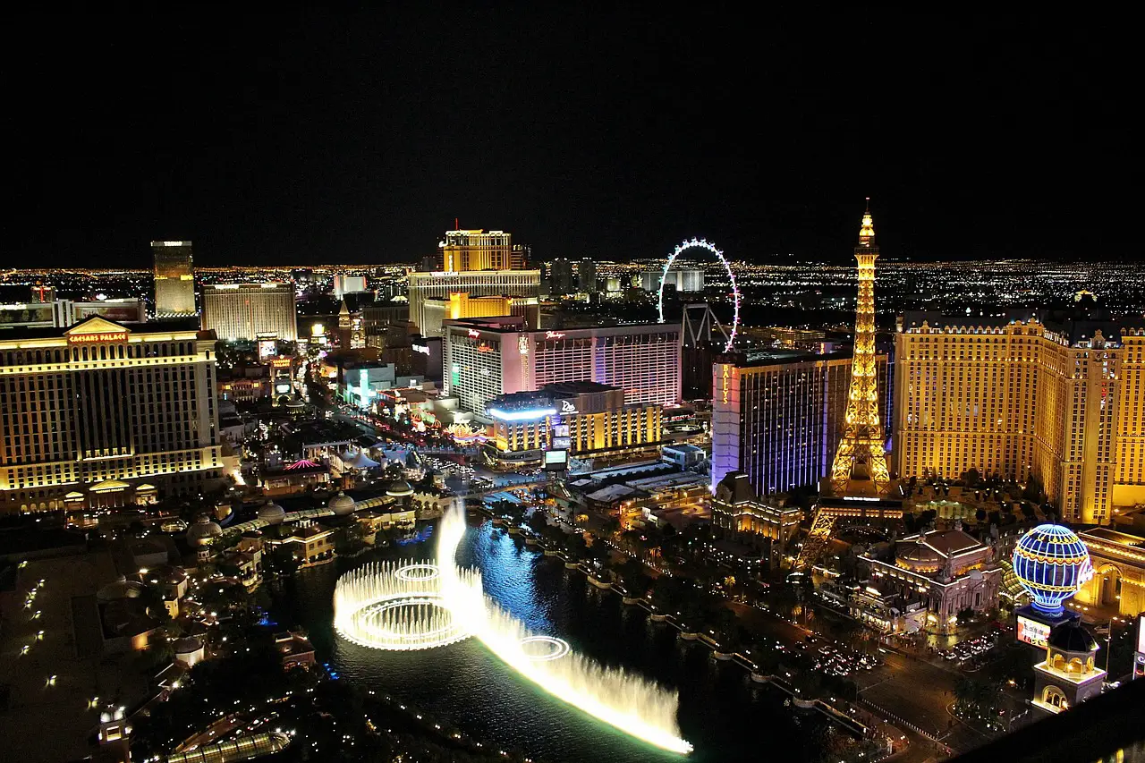 Las Vegas Strip at night with illuminated hotels, Eiffel Tower replica, and dancing fountain show.