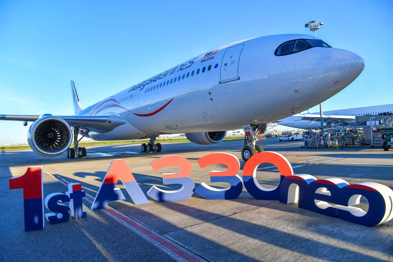 Malaysia Airlines’ first Airbus A330neo parked on the tarmac, with a “1st A330neo” sign prominently displayed in front of the aircraft under a bright blue sky.