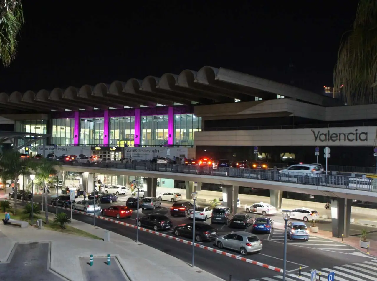 Valencia Airport at night with cars and a bus at the entrance.