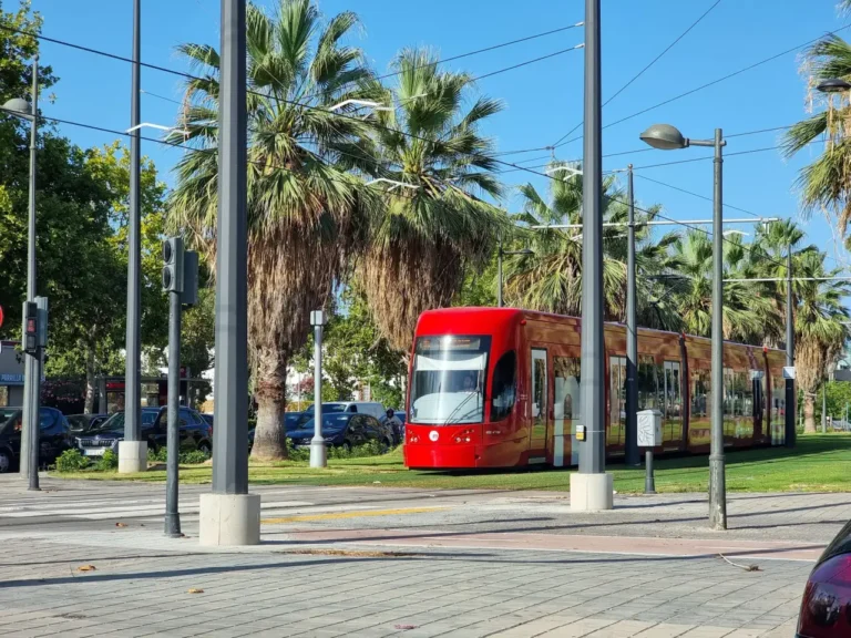 Spain Travel And Tourism News 14 Red tram in Valencia on a sunny day, with palm trees in the background.