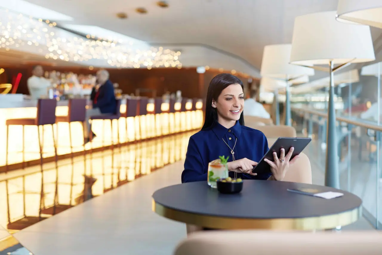 A woman using a tablet while seated in a stylish airport lounge bar.